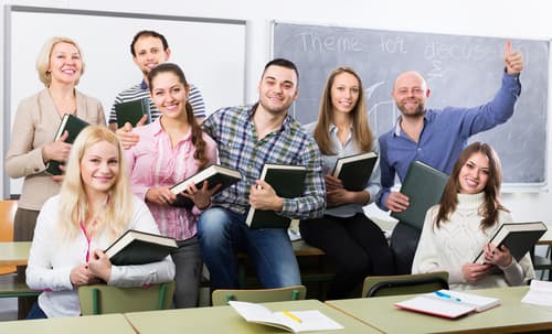 A group of adults holding books together in a classroom
